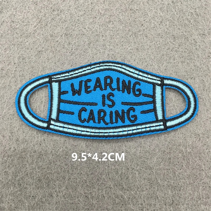 Blue fabric face mask embroidered with the text Wearing is Caring