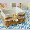 A woven jute rope basket lined with white fabric and lace, displayed on a blue and white chevron patterned cloth.