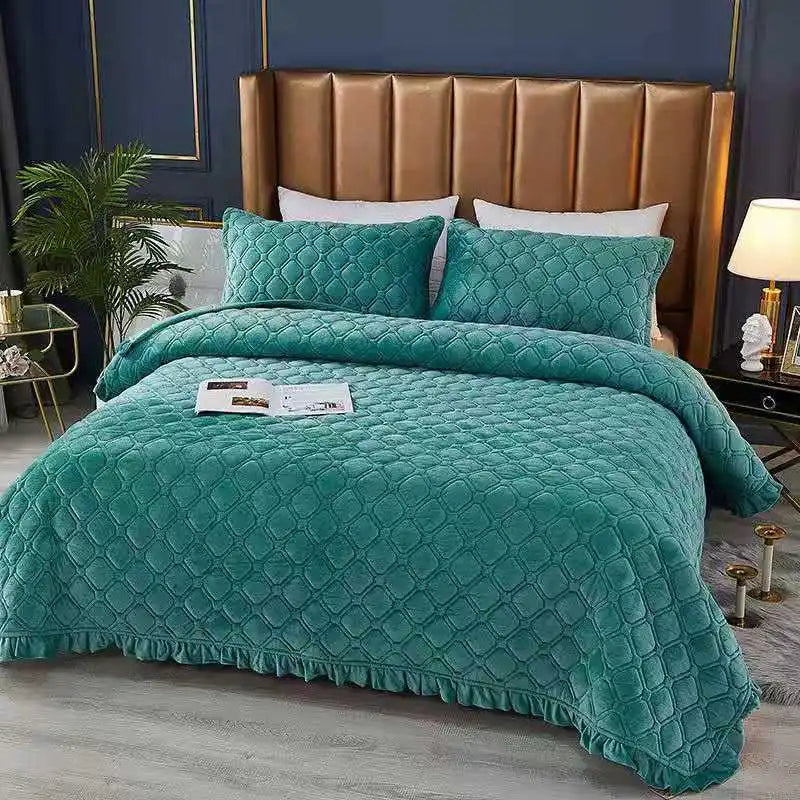A teal quilted velvet bedspread is displayed on a bed with a brown leather headboard.
