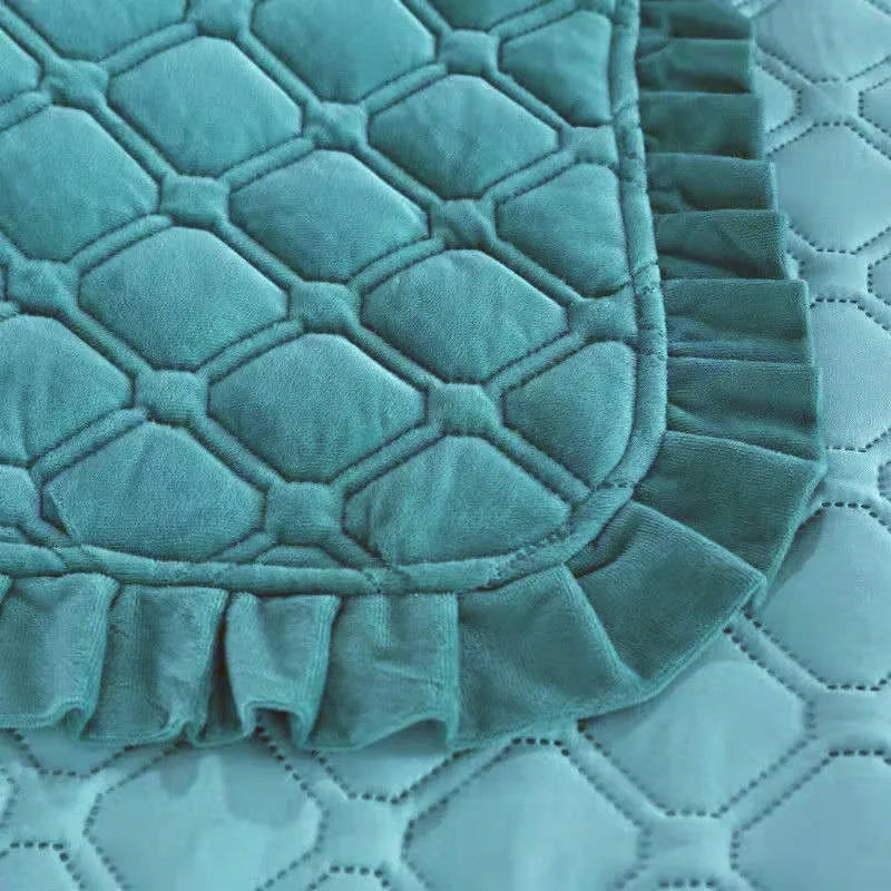 A teal crystal velvet quilted bedspread with a ruffled edge lying on a white quilted surface.
