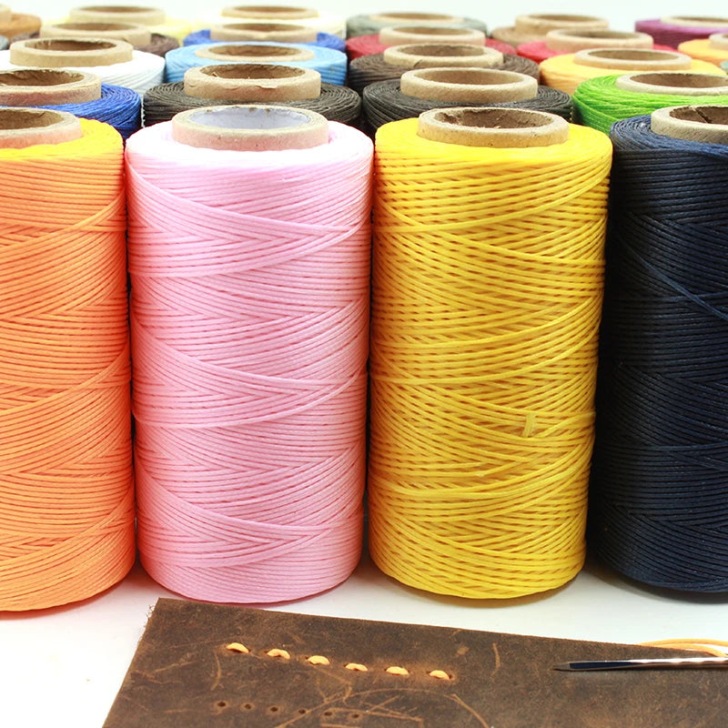 Rolls of waxed thread in various colors including orange pink yellow and dark blue stacked on a brown leather surface