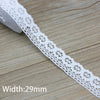 A white cotton embroidered lace trim is shown on a wooden surface, displaying its intricate pattern and width of 29mm.
