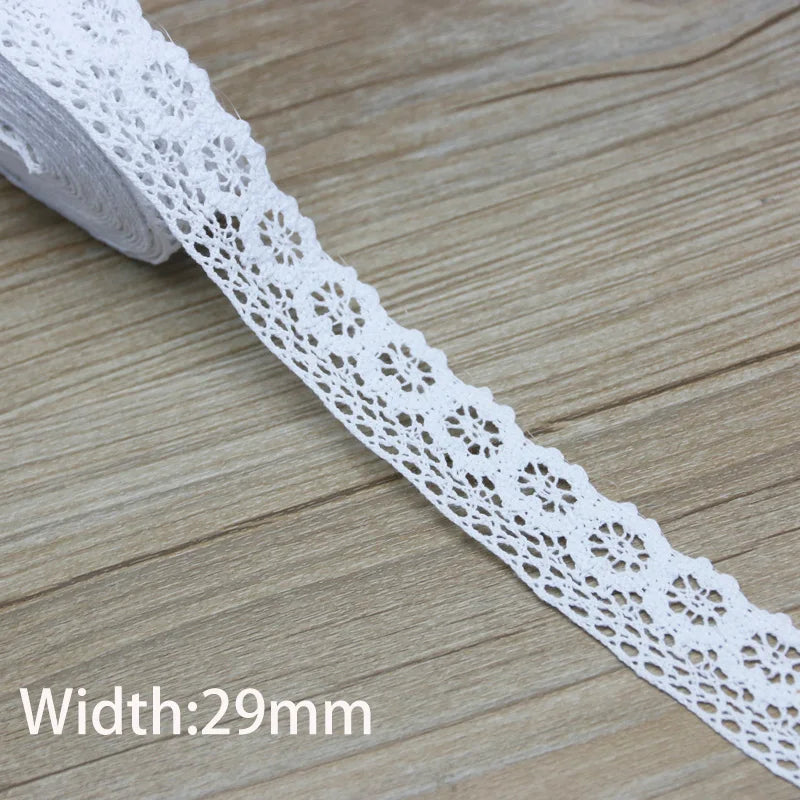 A white cotton embroidered lace trim is shown on a wooden surface, displaying its intricate pattern and width of 29mm.