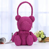 A handmade crocheted teddy bear in magenta yarn sitting on a white surface.