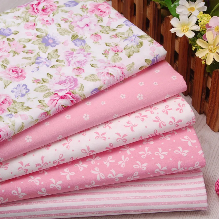 A stack of pink floral and stripe cotton twill fabric rolls with a wooden basket in the background.