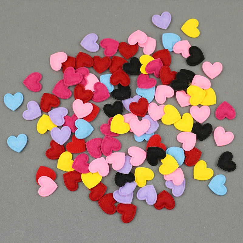 A scattered collection of colorful felt heart appliques in shades of pink, red, yellow, purple, and black on a gray backgroun