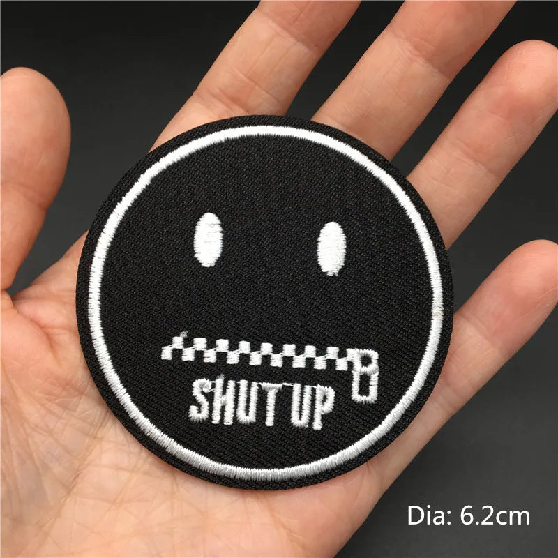 Black embroidered punk badge with a face and the text SHUT UP on a hand