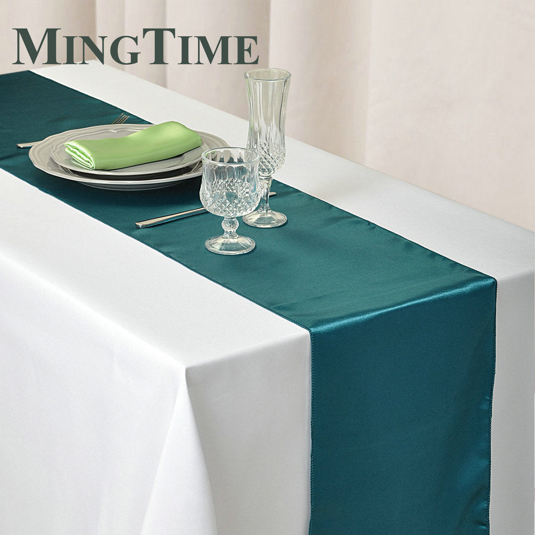 Elegant teal satin table runner set with silverware and glassware on a white tablecloth
