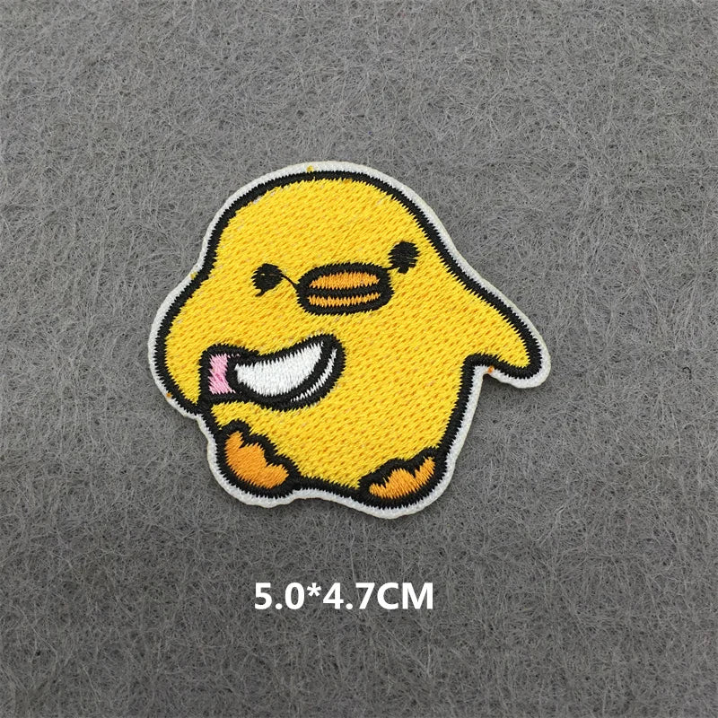 A yellow embroidered patch of a cartoon chick on a gray fabric background.