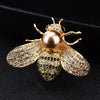A gold-toned crystal bee brooch featuring a pearl accent and detailed diamond-like wings.
