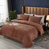 A brown crystal velvet quilted bedspread draped over a bed with a padded headboard.