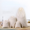 A set of natural beige cotton drawstring gift bags resting on a woven mat.
