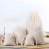 A set of natural beige cotton drawstring gift bags resting on a woven mat.
