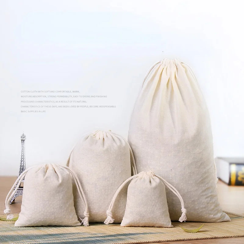A set of natural beige cotton drawstring gift bags resting on a woven mat.