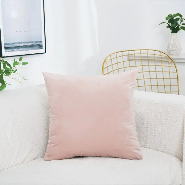 A soft pink velvet decorative cushion cover resting on a white sofa next to a gold wire chair.