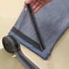 A hand is holding a black self-adhesive hem tape used for no-sew fabric repair on denim pants.