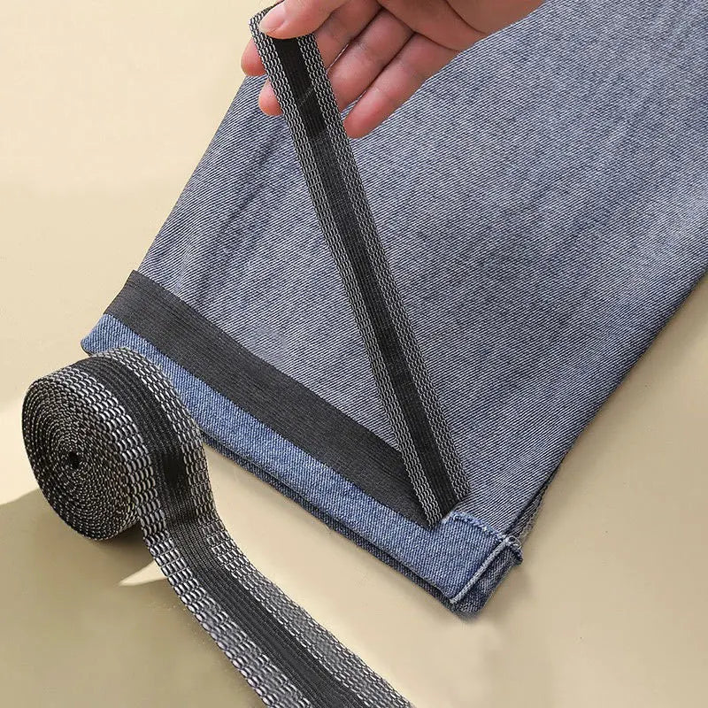A hand is holding a black self-adhesive hem tape used for no-sew fabric repair on denim pants.