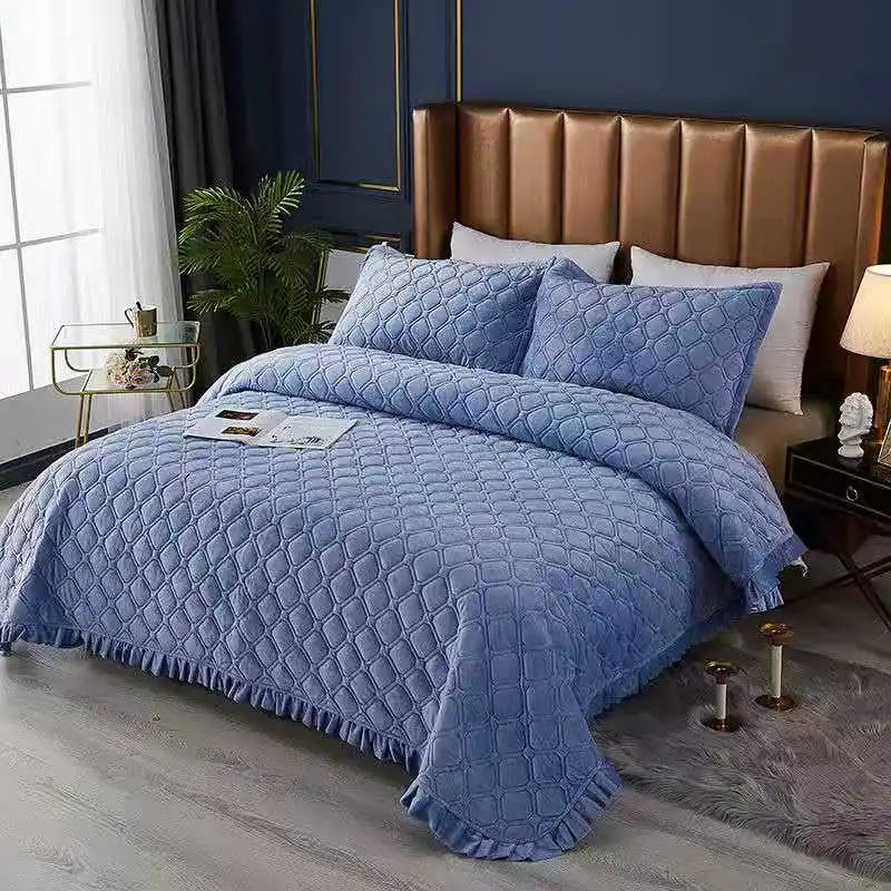 A blue crystal velvet quilted bedspread draped over a bed with a brown leather headboard.