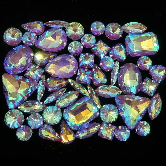 A collection of iridescent and faceted gemstone rhinestones in shades of purple, blue, and green.