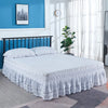 A white bed with an embroidered ruffle skirt is shown in a bright room.