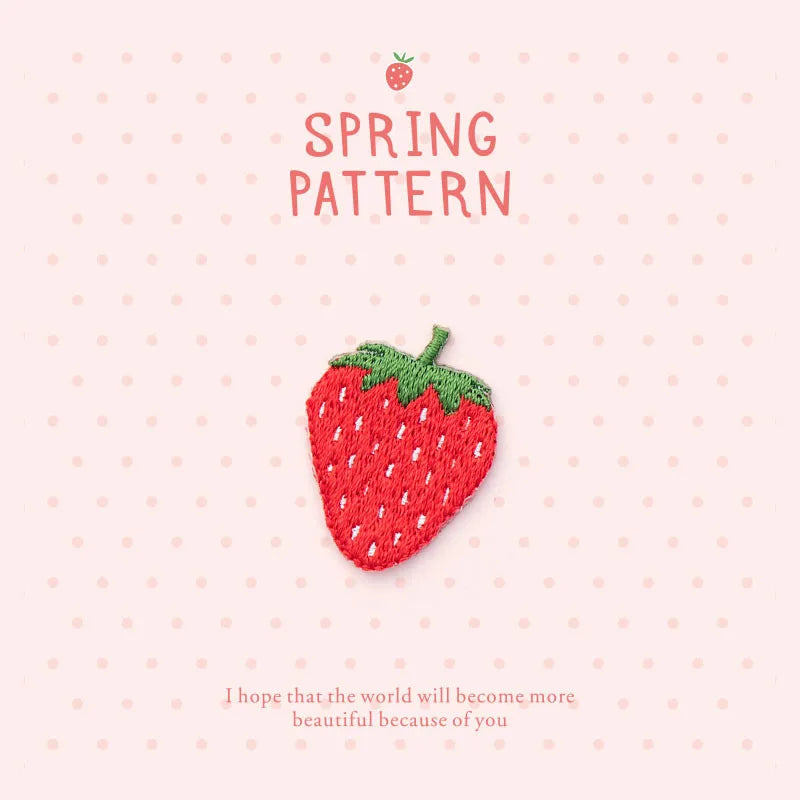 A pink patterned fabric featuring a red strawberry embroidery patch and text wishing beauty.