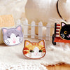 Handmade embroidered cat iron-on patches featuring gray and orange cats on a beige fabric background.