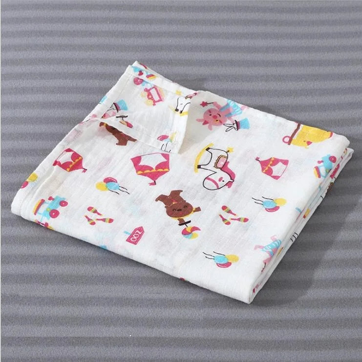 A white cotton muslin swaddle blanket featuring colorful animal and geometric designs.