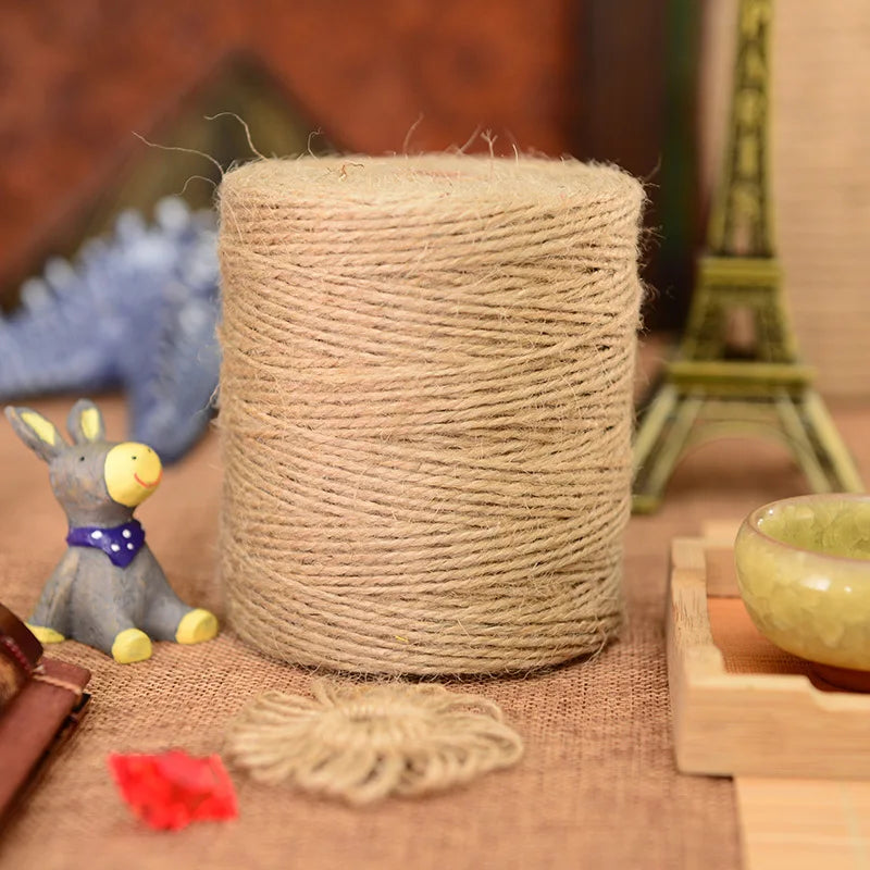 A large spool of natural beige hemp jute rope lying on brown fabric with a small yellow toy and a green Eiffel Tower in the b