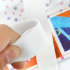 A hand is gripping a white adjustable bed sheet gripper or fastener, shown next to colorful fabric.