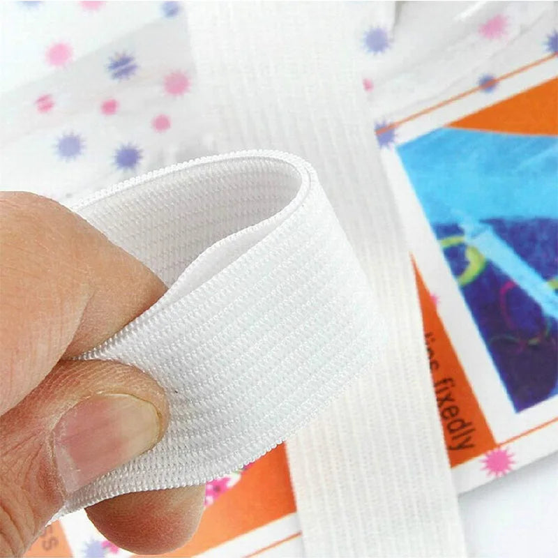 A hand is gripping a white adjustable bed sheet gripper or fastener, shown next to colorful fabric.
