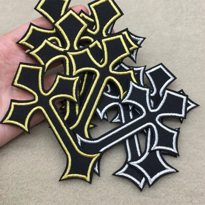 Black and gold embroidered cross applique patches scattered on a light background.