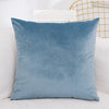 A solid blue velvet decorative cushion cover resting on a white sofa.