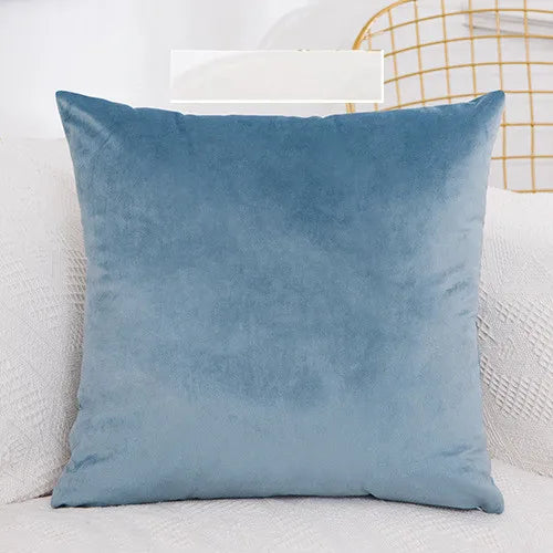 A solid blue velvet decorative cushion cover resting on a white sofa.