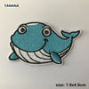 A light blue embroidered patch of a smiling whale with white details.
