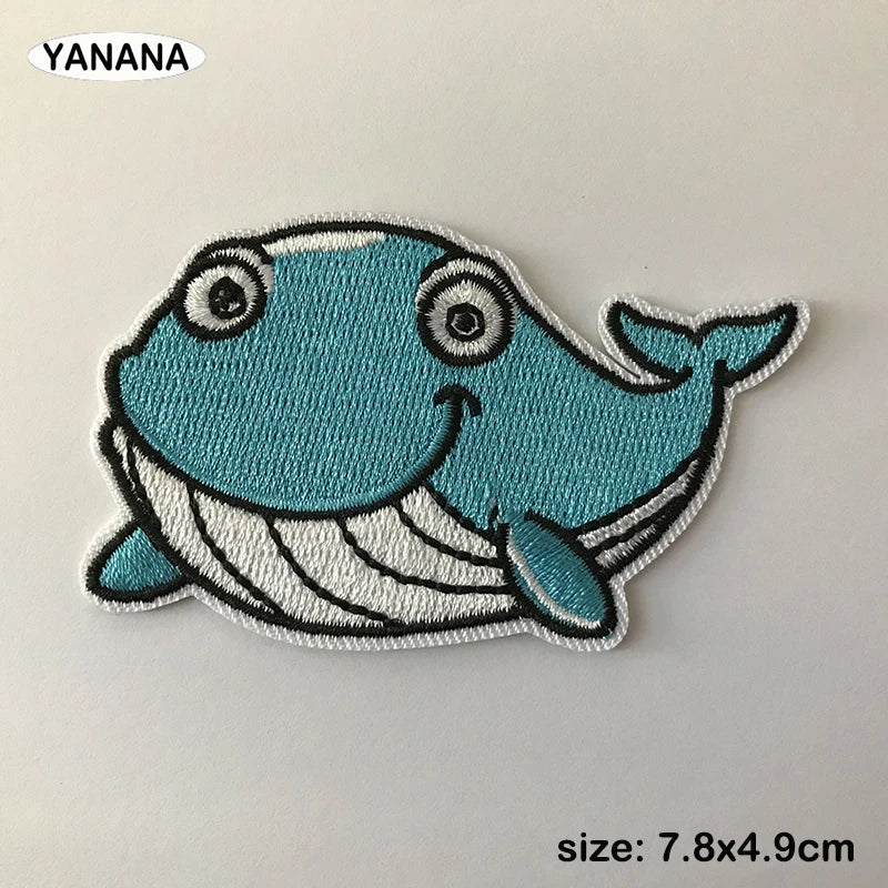 A light blue embroidered patch of a smiling whale with white details.