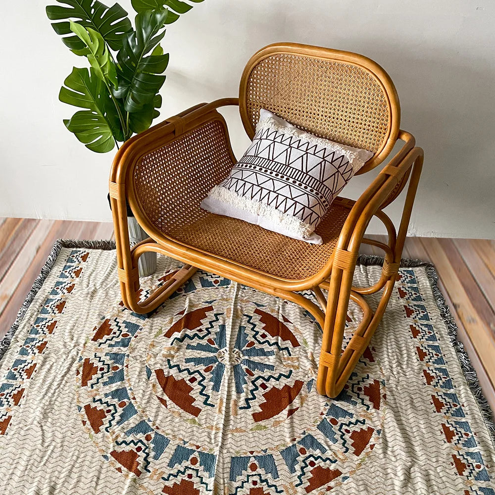 A woven wooden chair with a cushion sits on a patterned rug, next to a green plant.