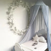 A light blue sheer canopy mosquito net draped over a white bed with soft lighting.