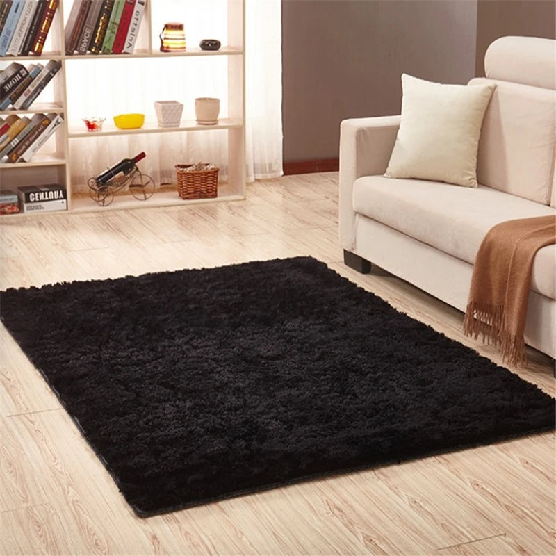 A black plush throw rug is placed on a light wood floor in front of a white sofa and shelving unit.