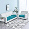 A white stretch sofa seat cushion protector slipcover with teal cushions on a light blue wall.