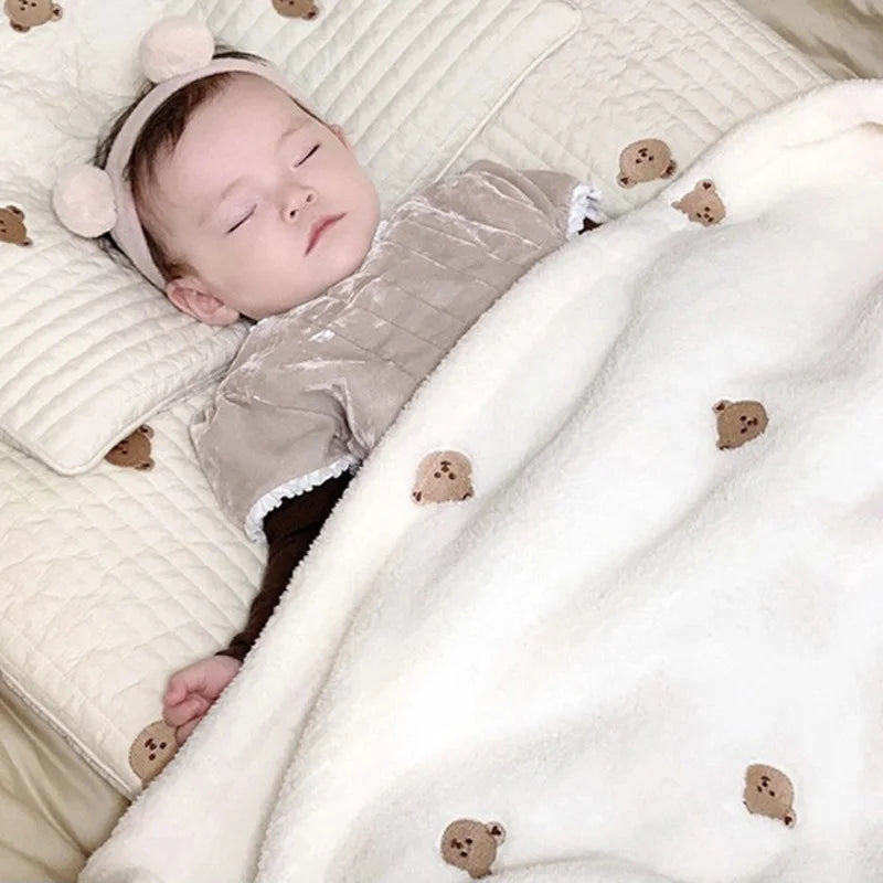 A newborn baby sleeping peacefully under a soft coral fleece flannel blanket with small teddy bear appliqués.
