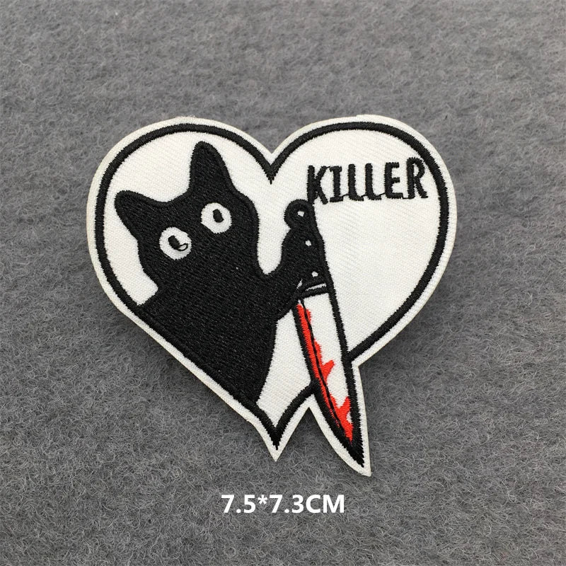A black cat silhouette with claws and a knife is embroidered inside a heart-shaped patch with the word KILLER above it.