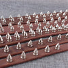 A row of brown leather punk screw back studs and spikes laid out on a gray surface.