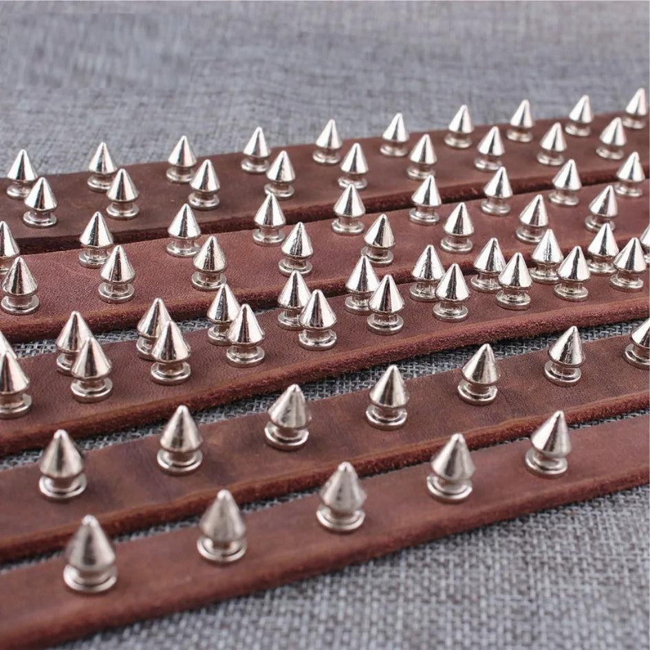 A row of brown leather punk screw back studs and spikes laid out on a gray surface.