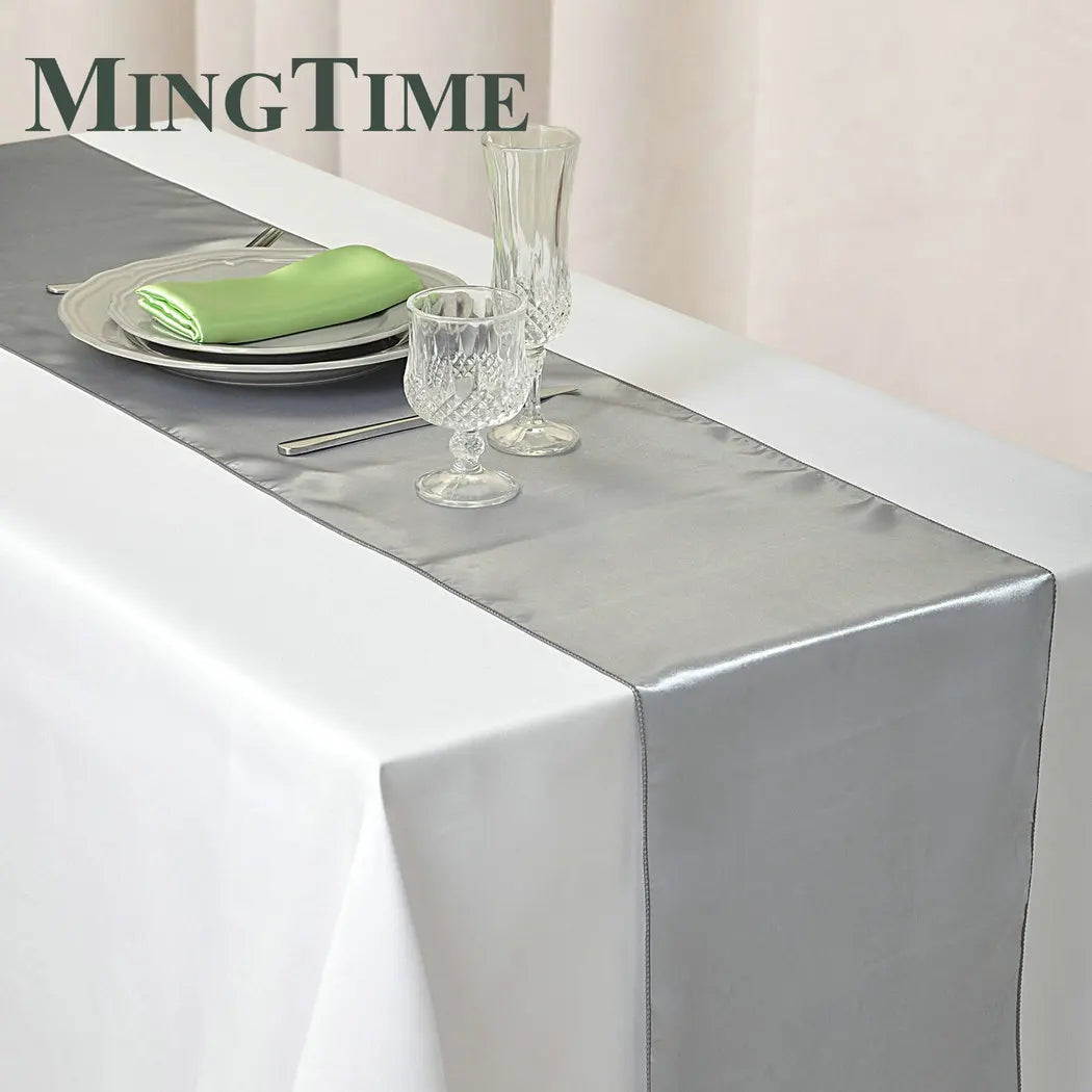 Elegant satin gray table runner set with green napkin and glassware on a white tablecloth