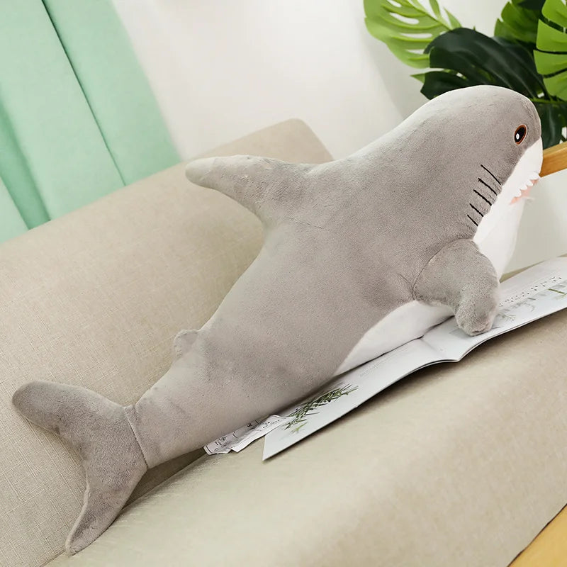 A gray giant shark plush toy lying on a light-colored sofa next to some papers.