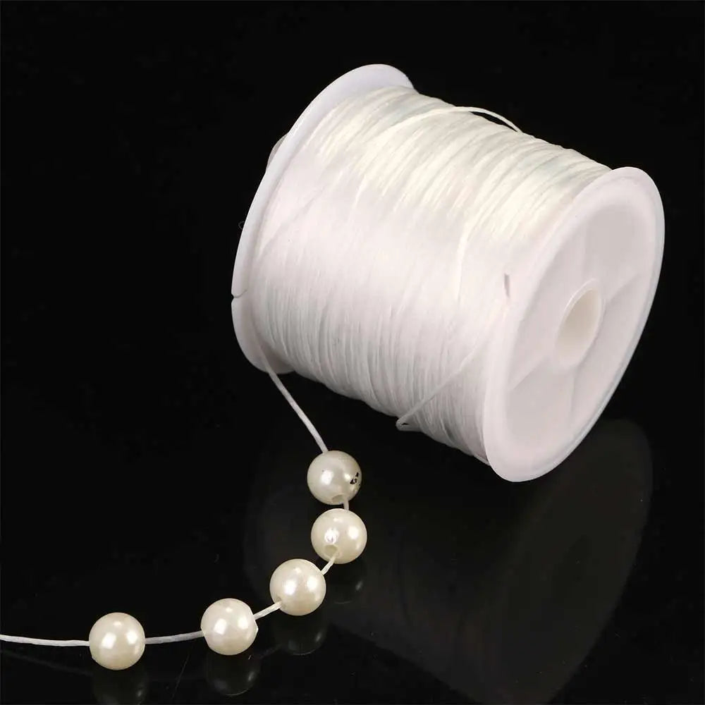 White flat elastic beading thread wound on a spool with a string of pearls extending from it.