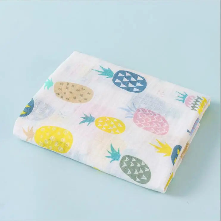 A folded white cotton muslin swaddle blanket featuring a pattern of colorful fruits like pineapple, kiwi, and strawberry.