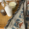 A bohemian geometric throw blanket draped next to a white candle and glass, resting on a woven tray.