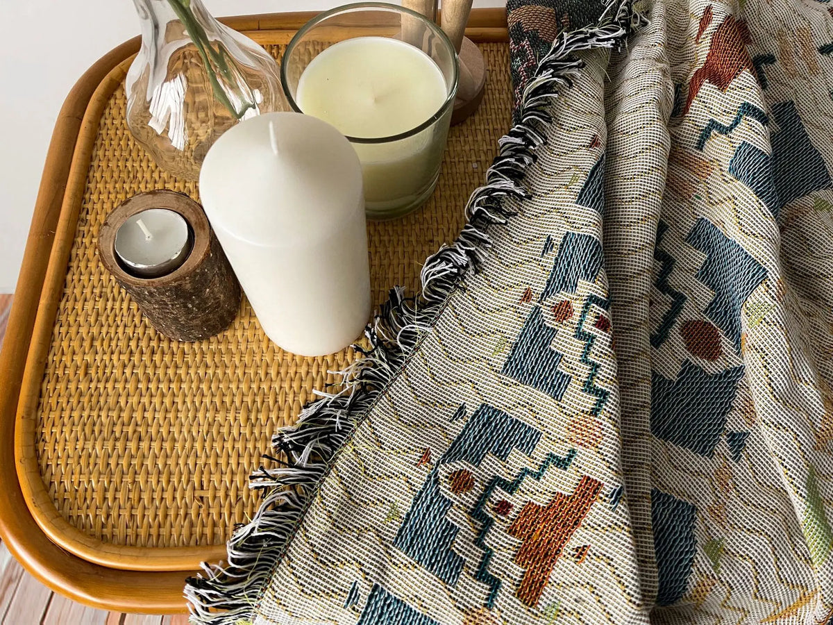 A bohemian geometric throw blanket draped next to a white candle and glass, resting on a woven tray.