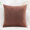 A solid brown velvet decorative cushion cover resting on a white sofa.